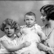 Princess Elizabeth holding Princess Margaret as a baby, watched on by the Queen Mother