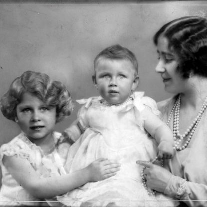 Princess Elizabeth holding Princess Margaret as a baby, watched on by the Queen Mother
