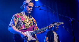 Italian funk guitarist and influencer Giacomo Turra performs live in a bright yellow, black and pink animal print Hawaiian shirt and plays a dark pink Mayones Aquila S-style electric guitar.