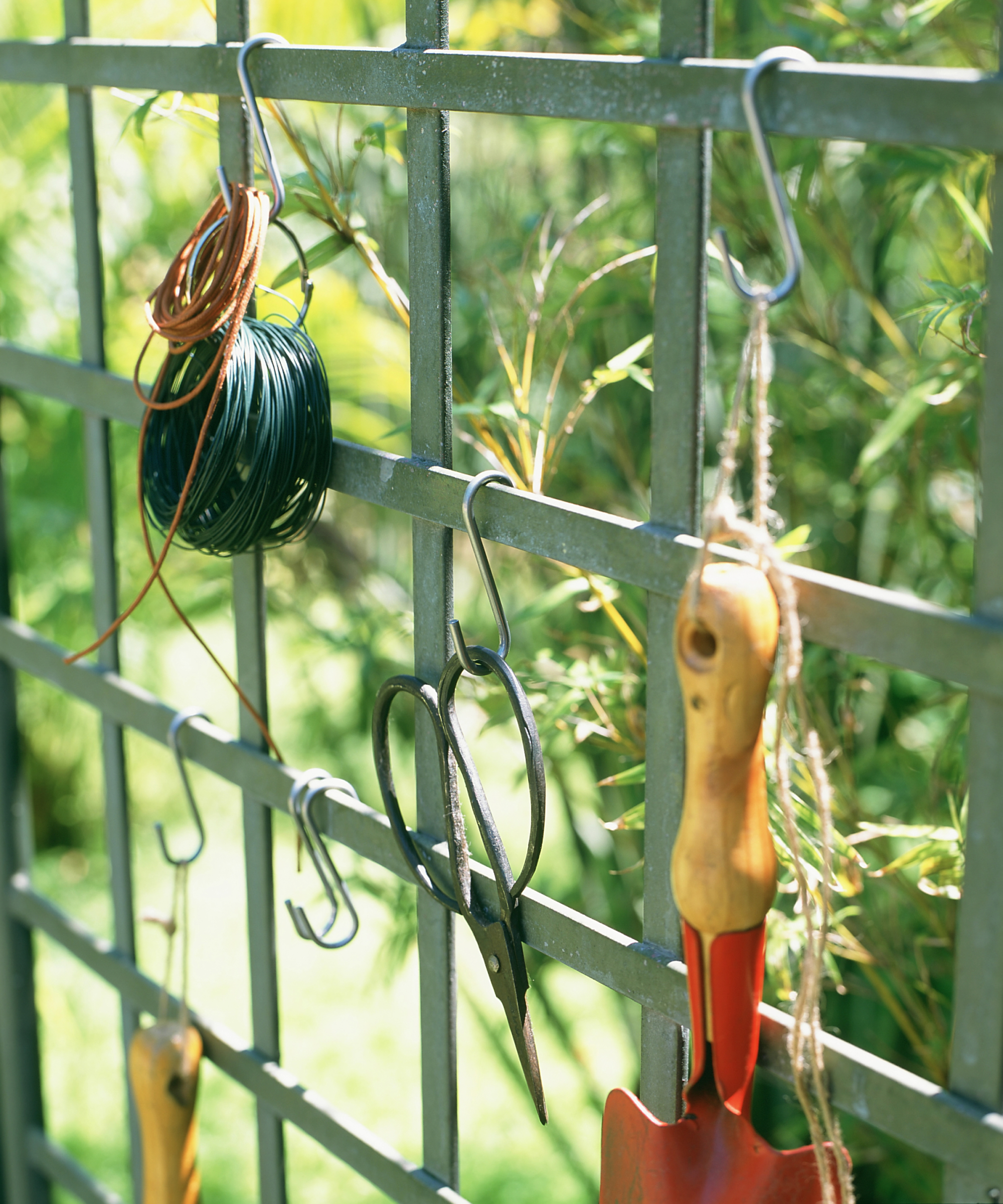 Gardening tools stored hanging on garden trellis.