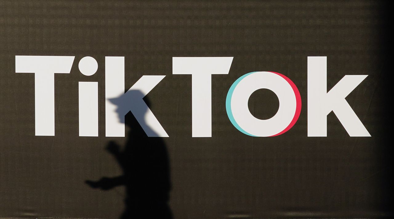 A young man holding a smartphone casts a shadow as he walks past an advertisement for social media company TikTok