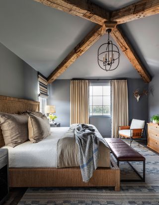 bedroom with grey walls and crossed exposed wooden rafters and stone walls