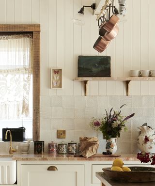 A white kitchen with textured white clay tiles and shiplap clad walls, with orange marble counter