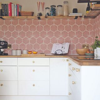 White kitchen cabinets with gold handles beneath pink tiles
