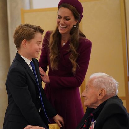 Princess Kate laughing putting her arm on George's shoulder, who is chatting to a WWII veteran