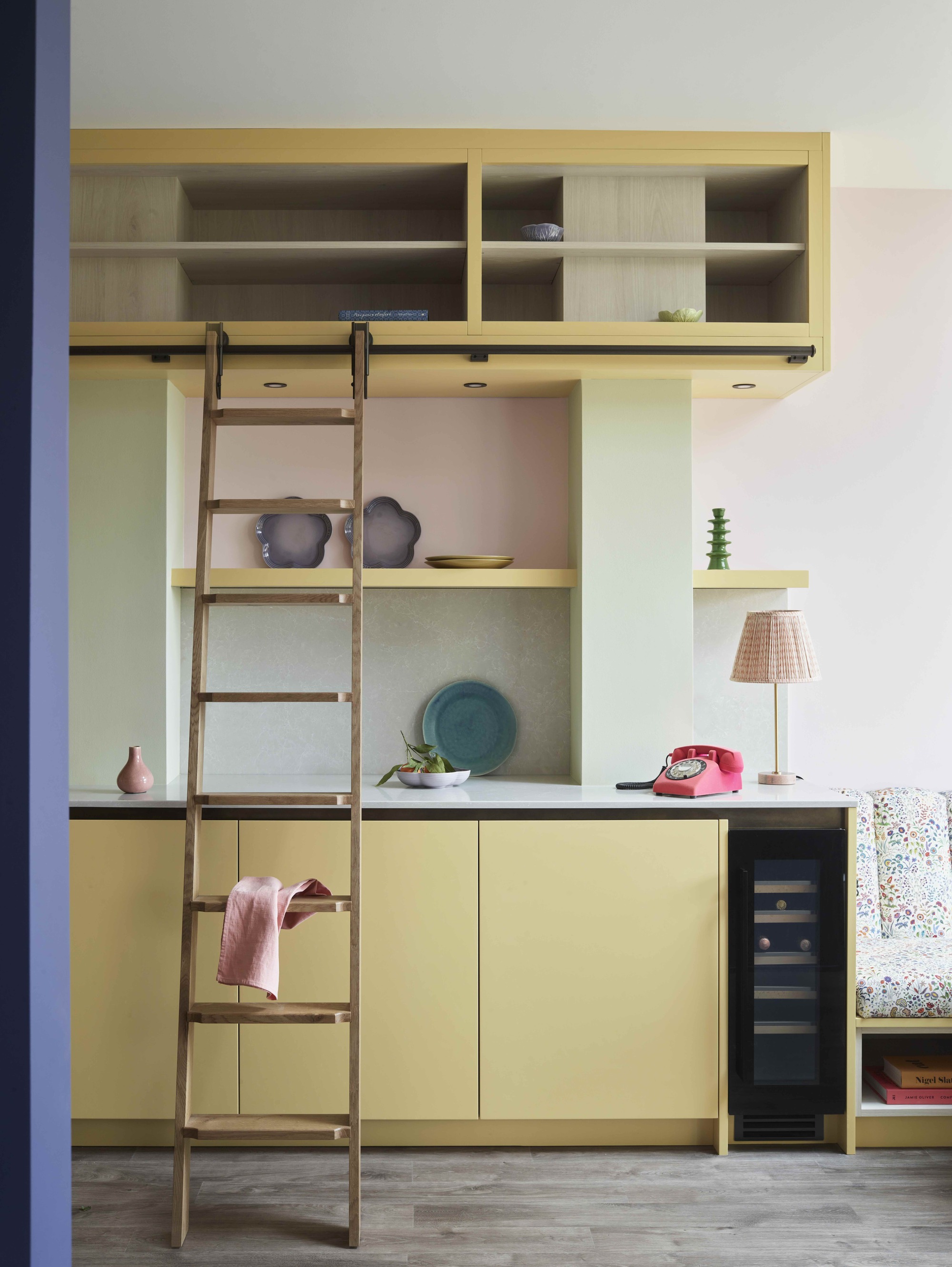yellow kitchen with pastel green and pink walls, with a kitchen ladder, bar fridge, and lamp on the counter
