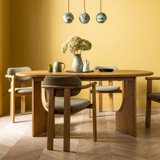 A yellow-painted dining room with an oval-shaped curved dining table and matching dining chairs