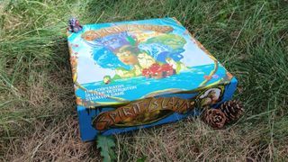 Spirit Island box lying on grass, with pinecones nearby
