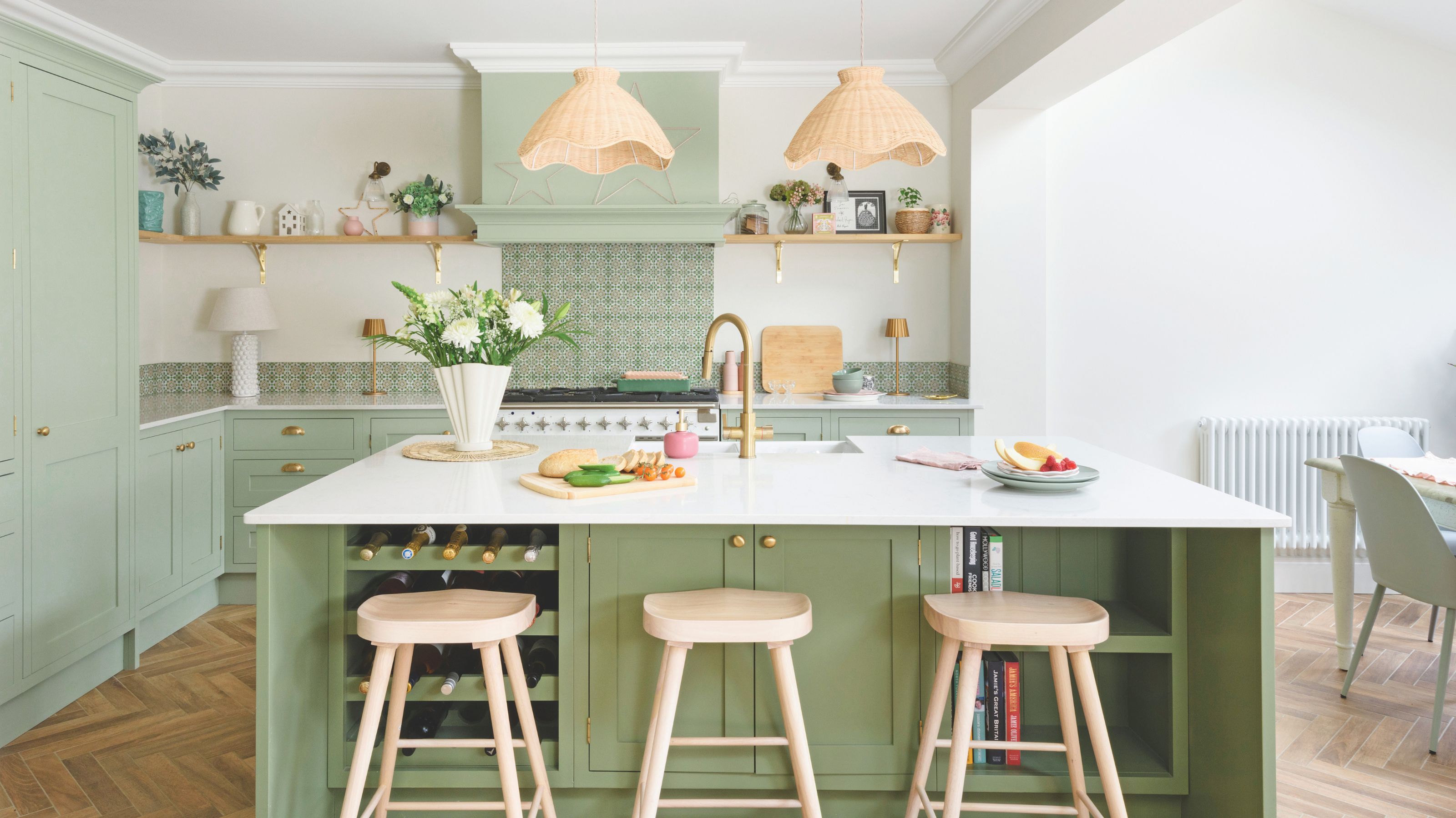 White painted kitchen with green cabinets and a matching green island with wooden stools around it