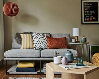 A small grey sofa with various colorful cushions and wooden table
