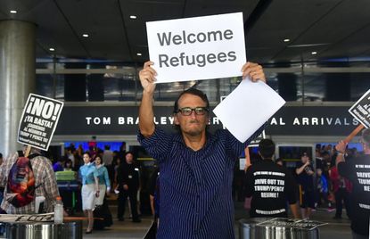 A man holds a sign that reads 'Welcome Refugees' on one side and 'Welcome Muslims' on the other as he walks the International Arrivals section at Los Angeles International Airport on June 29,