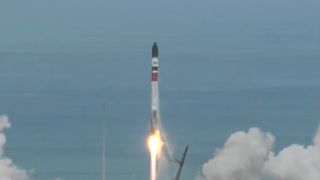 a white, green and red rocket launches into a blue sky.