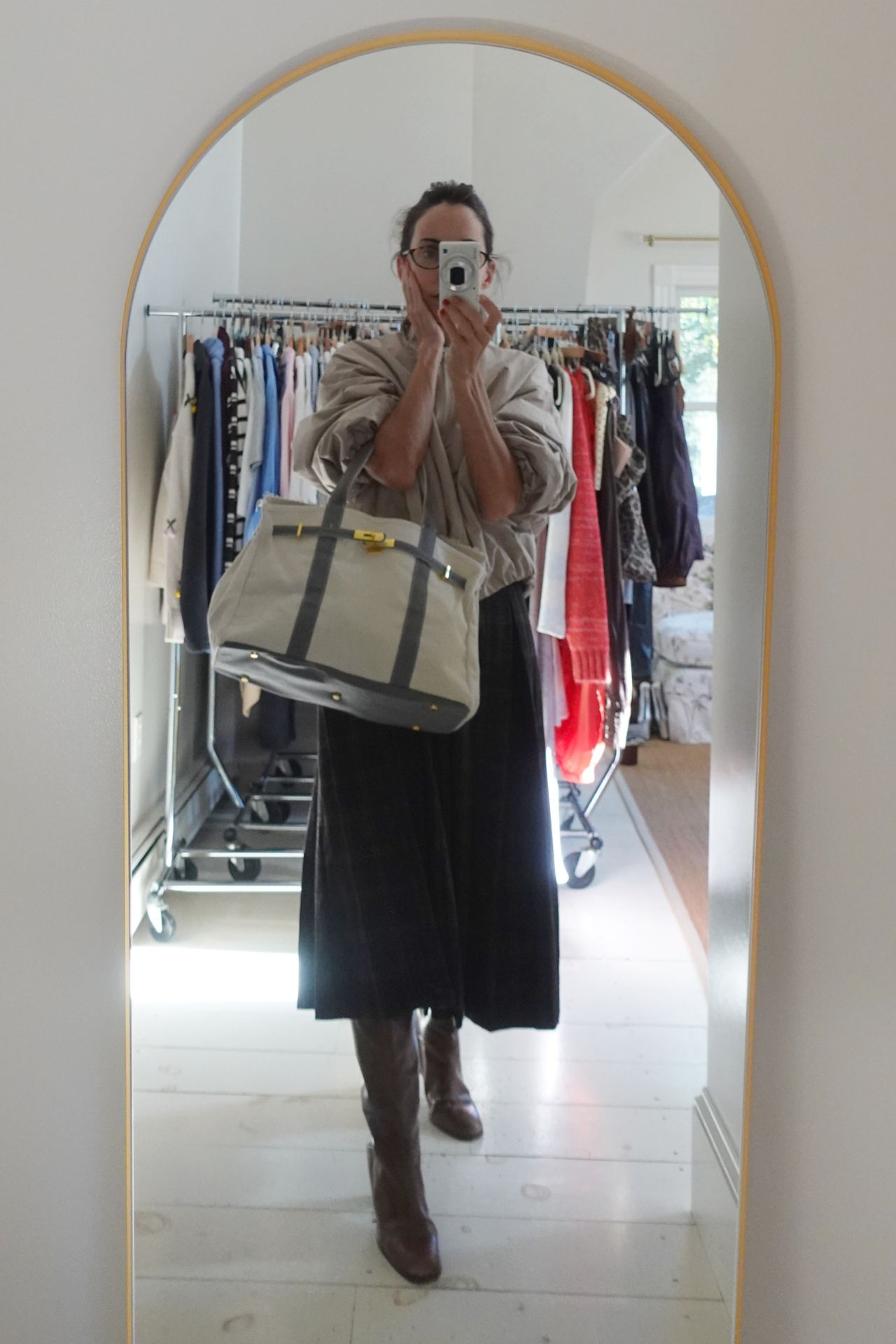 Larissa Mills wearing a tan windbreaker, black skirt, brown tall boots, and canvas and leather handbag.