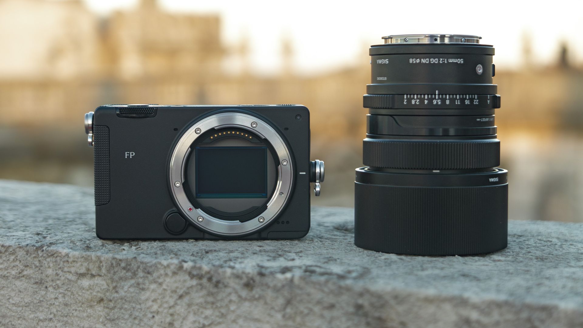Sigma FP2 mirrorless camera alongside the 50mm f/2 contemporary lens they are placed on a marble wall, at golden hour