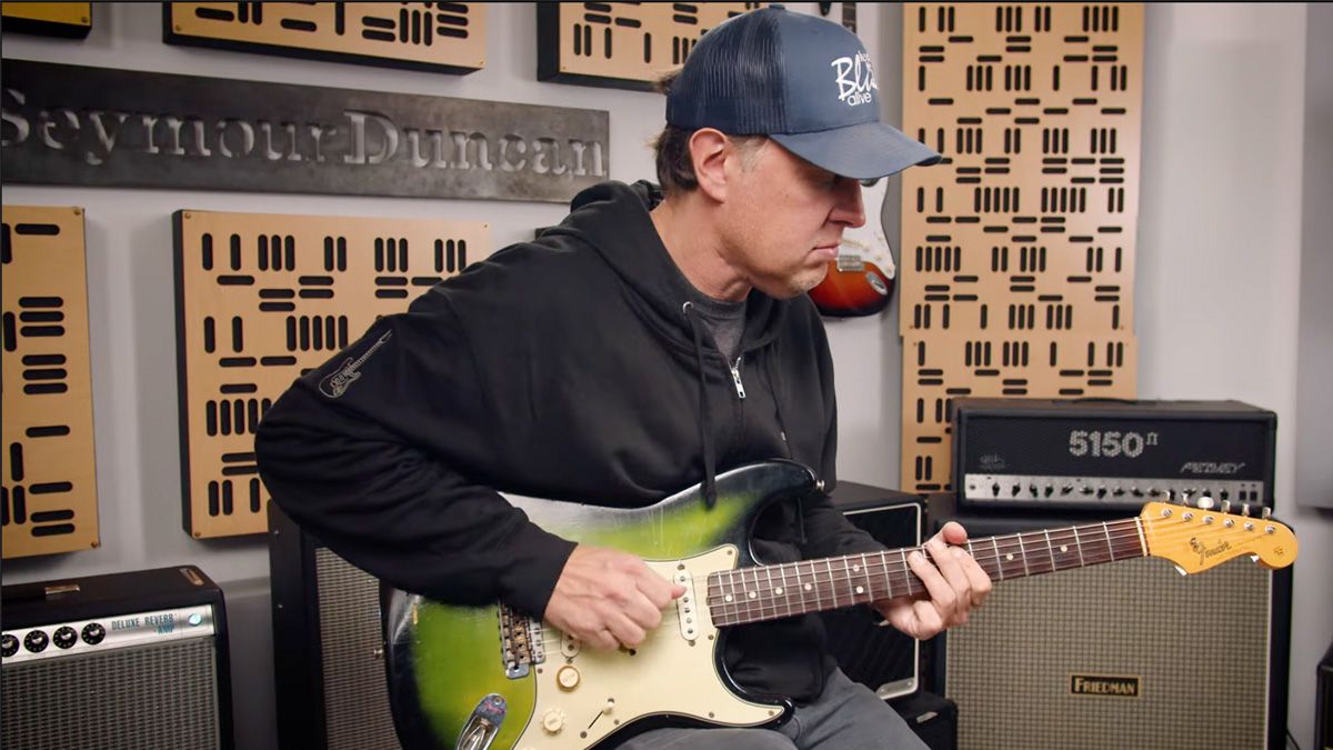 A still of Joe Bonamassa playing his 64 Greenburst Strat as he demos his new signature Seymour Duncan pickup set. Bonamassa wears a ballcap and a black hoodie. 