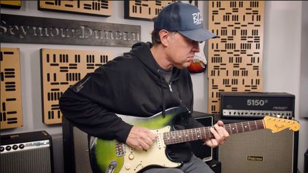 A still of Joe Bonamassa playing his 64 Greenburst Strat as he demos his new signature Seymour Duncan pickup set. Bonamassa wears a ballcap and a black hoodie. 