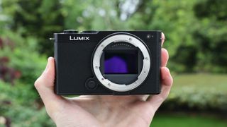 Panasonic Lumix S9 camera held in a hand in front of a green bush