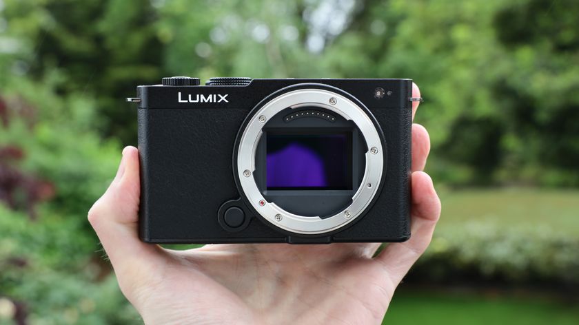 Panasonic Lumix S9 camera held in a hand in front of a green bush