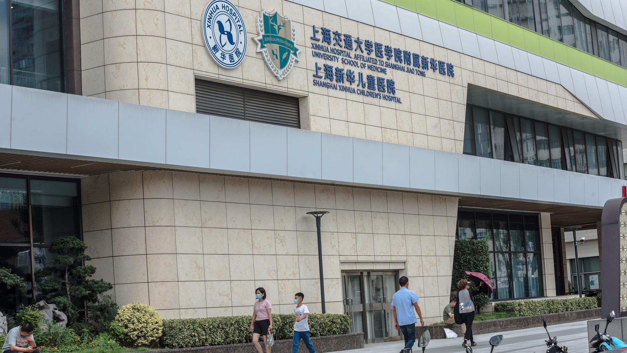 A tan building with Chinese characters on it is seen with people walking in front of it.