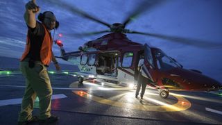 a helicopter spinning up on a ship at dusk with a person in front pointing to the sky