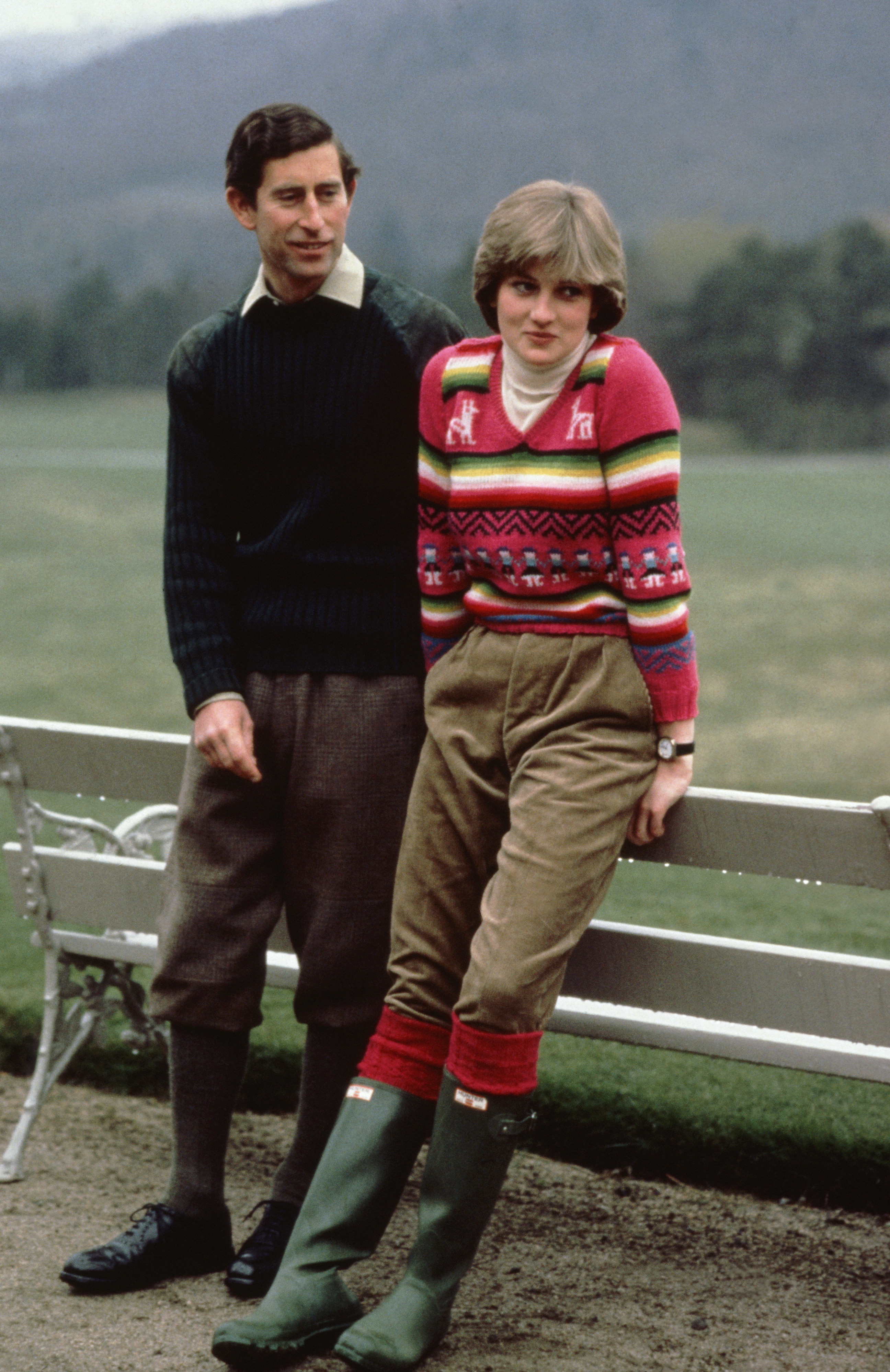 Prince Charles and Princess Diana leaning on a bench at Balmoral wearing sweaters