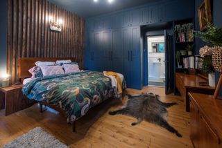 The master bedroom has a bear rug on the floor, wooden panelling behind the bed and overhead lights with wooden cabinets and cupboards