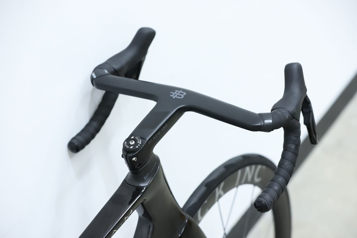 A Black Factor Ostro Vam leans against a white wall