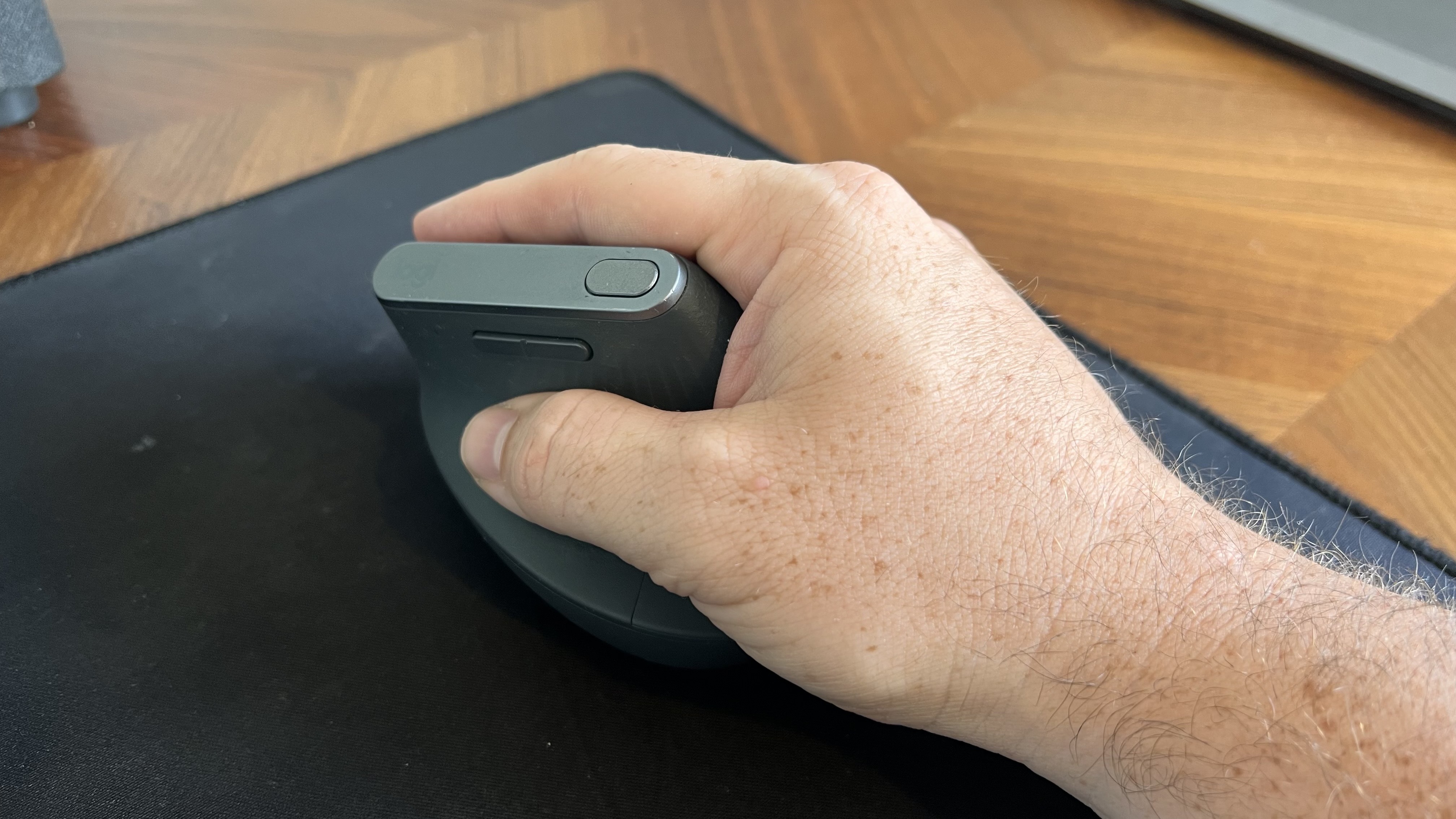 Close-up of a hand holding the Logitech MX Vertical ergonomic mouse in a natural handshake grip position on a black mousepad.