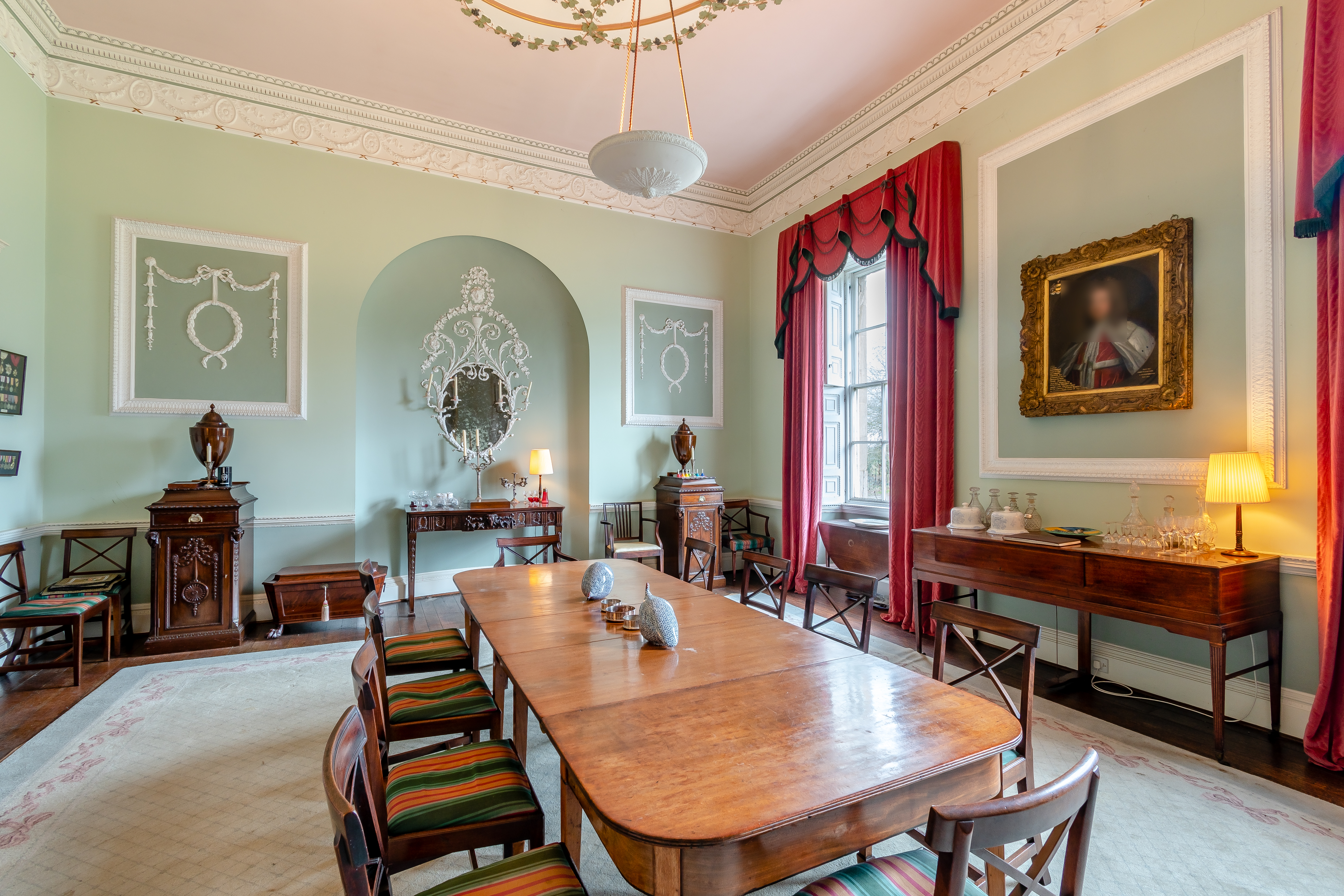 A dining room with a long dark wooden table and majestic red curtains