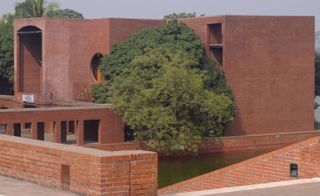 National Assembly Building of Bangladesh. A rectangle building with a facade of red bricks. There is a huge tree almost leaning on the building.