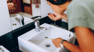 Woman brushing teeth before breakfast over sink in bathroom