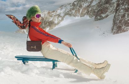 Woman in Gucci skiwear on sleigh in snow with mountains