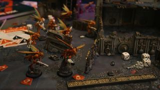 A group of Vespid Stingwing models on a battlefield strewn with model ruins, a themed ruler, and cards