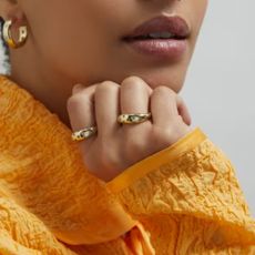 Woman in orange top wearing two Liberty rings and a set of earrings