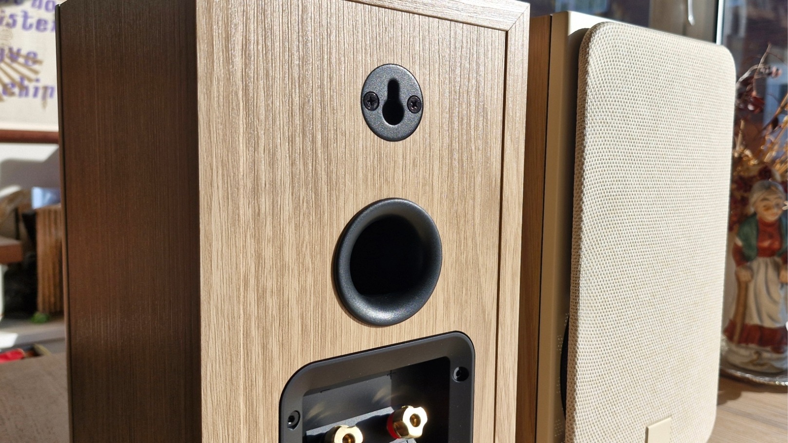 Dali Sonik 1 passive bookshelf speaker, one facing forwards and the other backwards to show the rear panel, on a wooden surface.