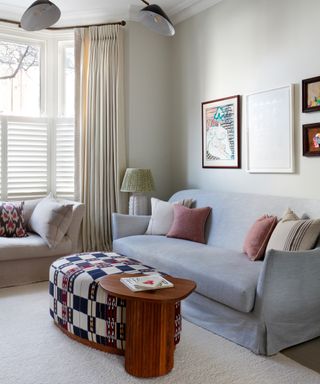 window treatment ideas living room, stylish living room with bay window half shutters, grey couch, bright footstool, cream drapes, artowrk, cushions