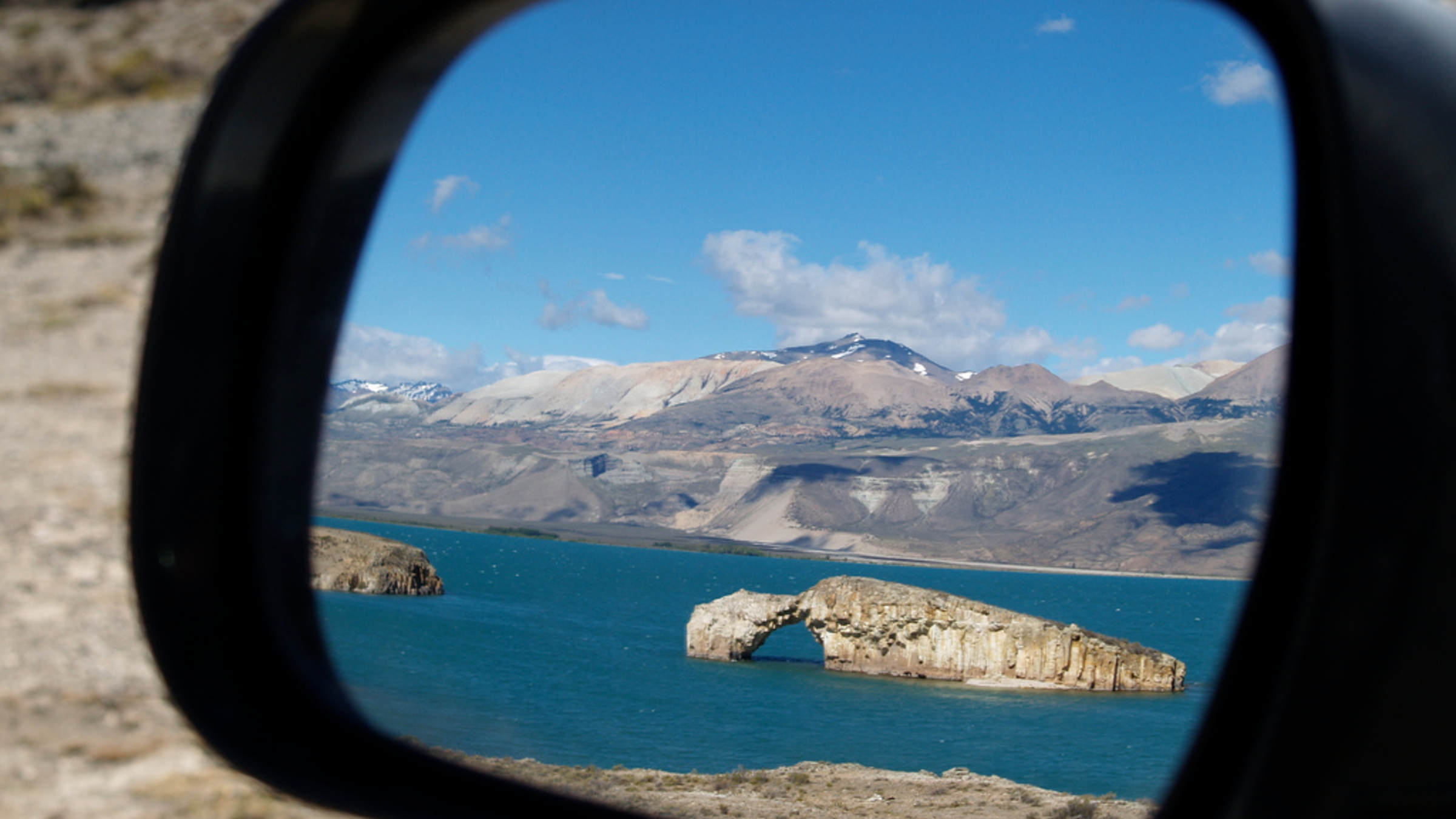 Lake Posadas and its famous rock arch reflected in a car wing mirror