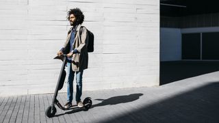 Man riding an electric scooter past a white brick wall
