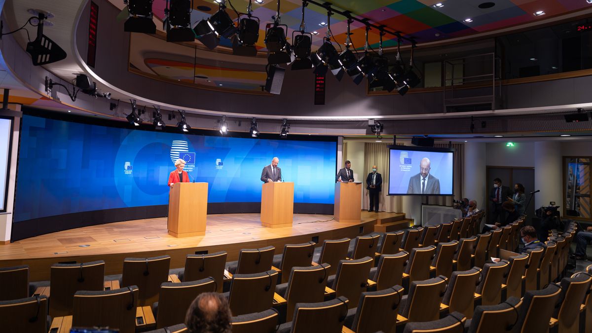 Two people at podiums on stage at the European Union in front of a curved, stunning blue LED display.