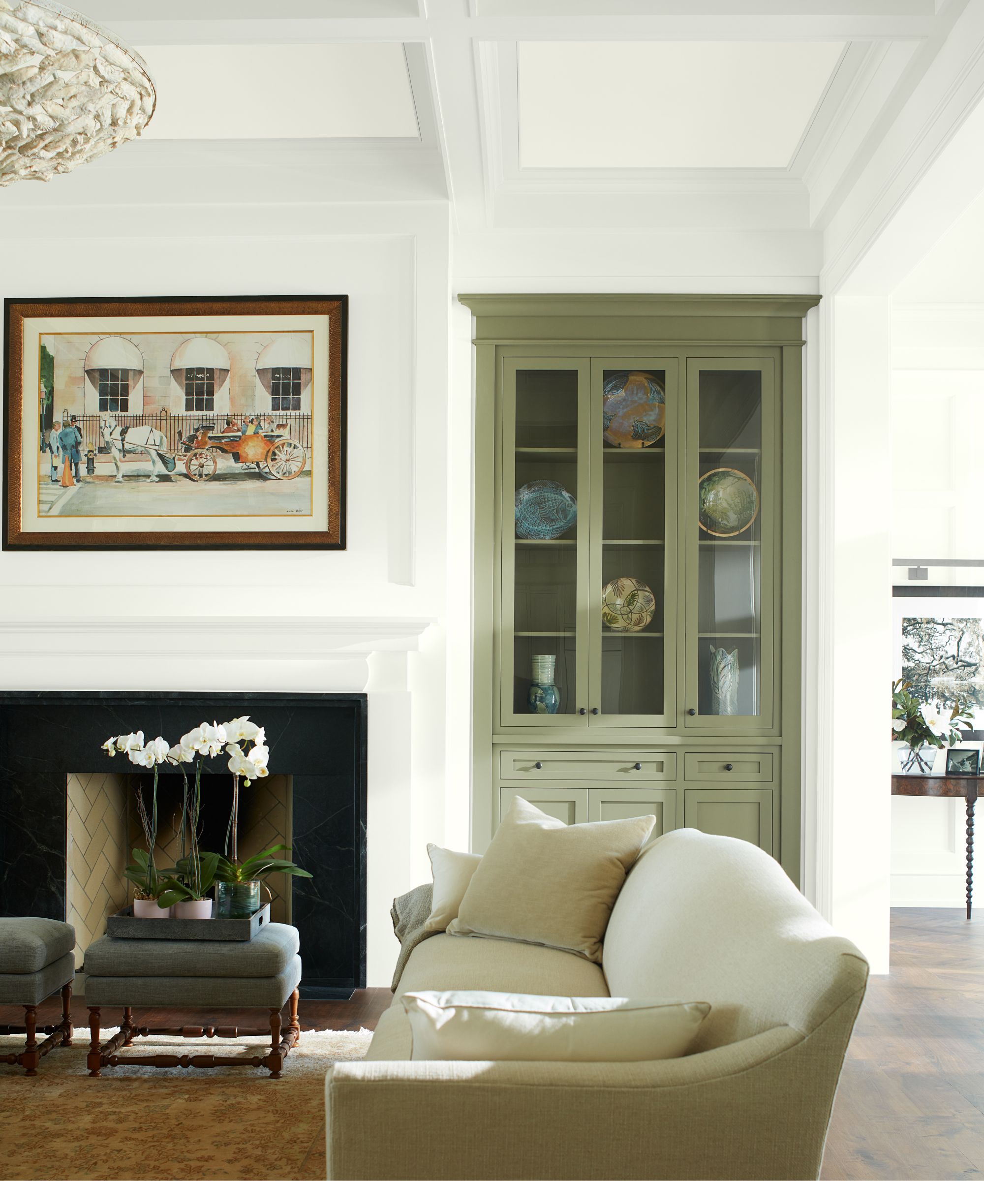 Transitional living room with white walls, large fireplace, a built-in cabinet painted in Rosemary Sprig by Benjamin Moore, a cream sofa, Persian rug, and a stool holding an orchid.
