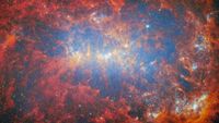 A photo of galaxy NGC 4449, with red and orange sparkling clouds