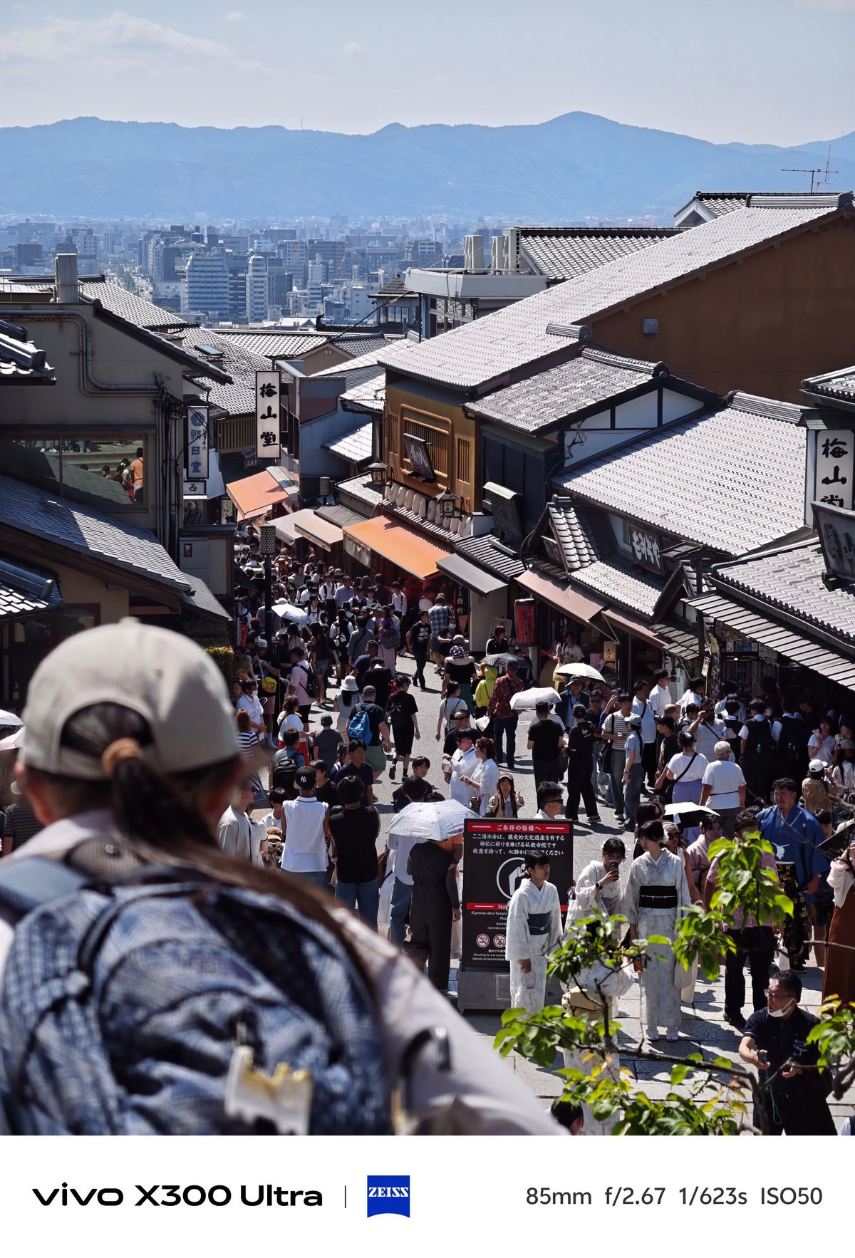 A high-angle view looking down a crowded hillside street lined with traditional tiled-roof buildings and shops.