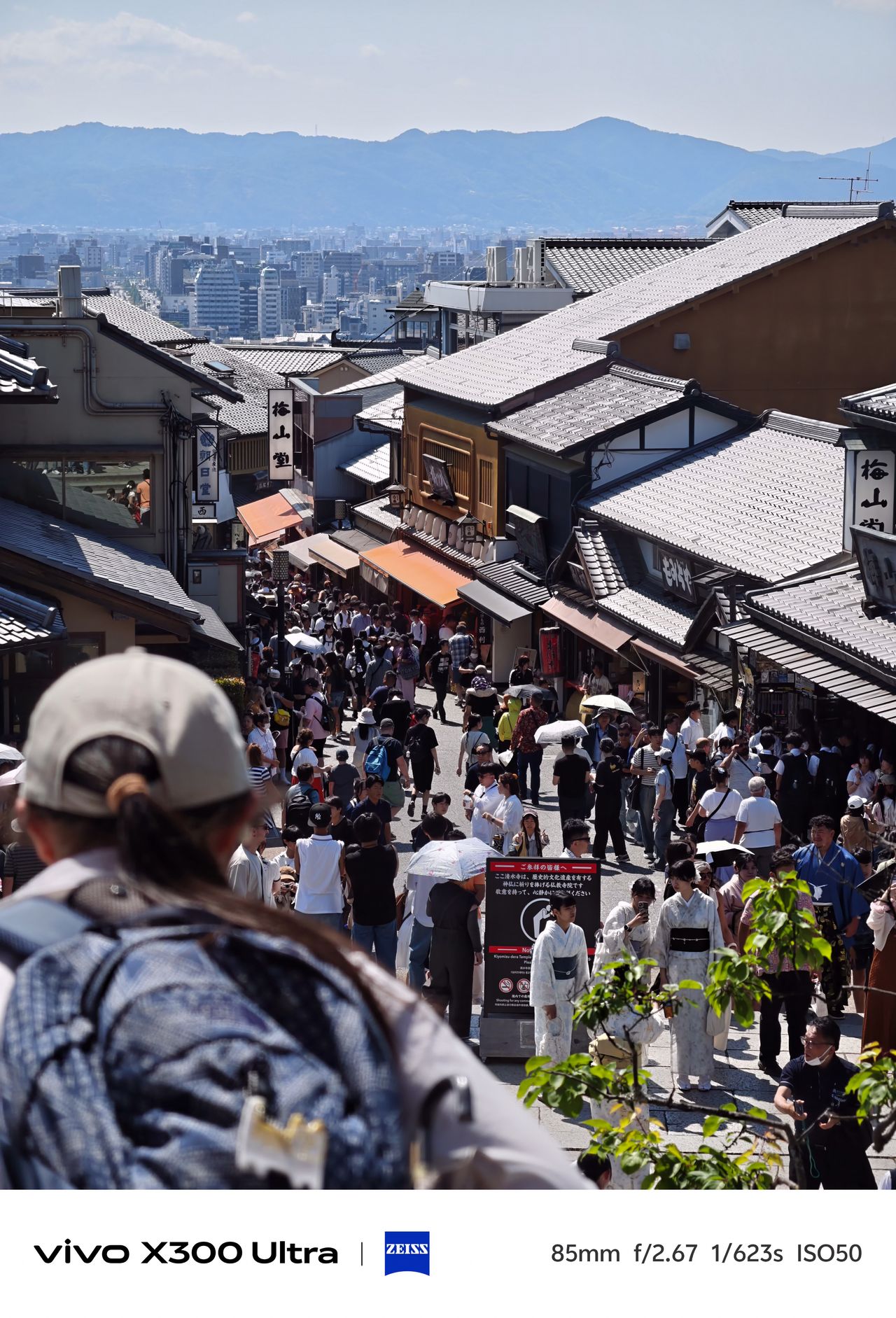 A high-angle view looking down a crowded hillside street lined with traditional tiled-roof buildings and shops.