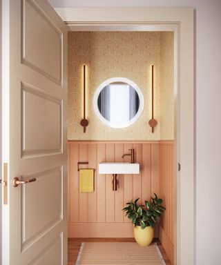 view into bathroom with pale terracotta panelled wall, wallpaper above, round mirror with two modern strip lights either side above small wall mounted white sink