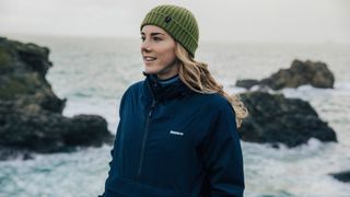 A woman wearing a beanie hat hikes by the sea