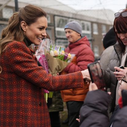 Princess Kate wearing an orange coat and shaking hands with fans