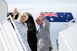 King Charles and Queen Camilla standing in front of a plane with an Australian flag and waving