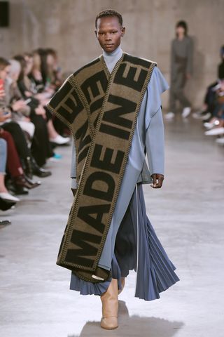 Model wears an oversized logo scarf with a blue skirt and top