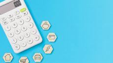 A calculator surrounded by six wooden hexagons, each with a picture symbolizing a part of a budget - piggy bank, credit card, home - and a bright blue background.