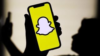 Snapchat logo displayed on a phone screen and silhouette of a woman with a phone in the background 